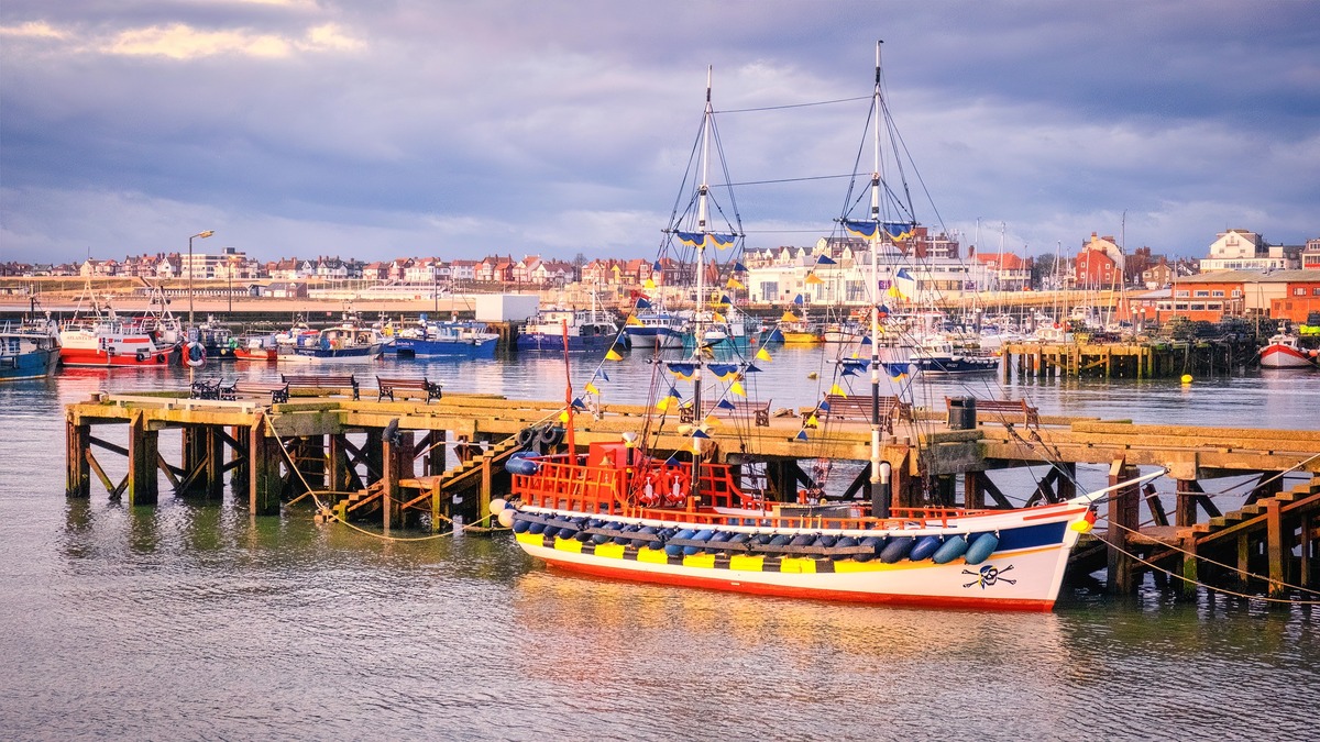 A colorful pirate-themed boat moored at Bridlington Harbour, with various fishing boats and the town's scenic waterfront in the background.